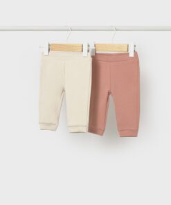 Two baby leggings in cream and dusty pink hanging on wooden hangers against a white background on a clothes rod