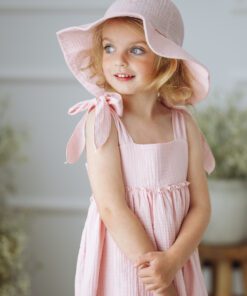 Young girl in a pale pink sun hat and matching pink dress looking to her left.