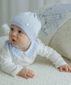 Baby lying on a soft white rug wearing a pale blue hat and matching collar looking alert to the side