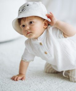 Baby crawling on a light carpet in a white outfit and hat with a cute animal face indoors