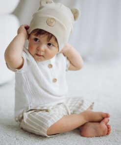 Baby wearing cream bear ear hat and white outfit sits on a light carpet