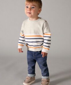 Toddler boy standing in a striped sweater and jeans looking to the side against a neutral gray background