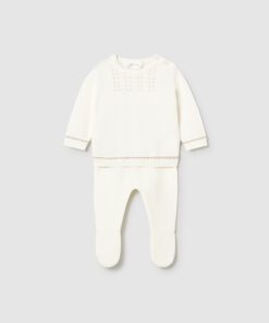 White knit footed baby romper with decorative chest stitching and a shoulder button opening on the top piece