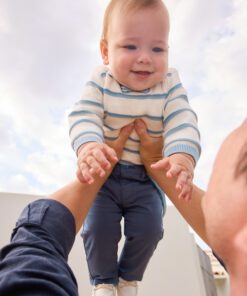 Baby being lifted into the air by two hands outdoors with a blue sky and clouds behind