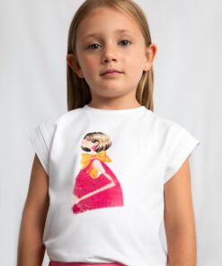 Young girl facing the camera wearing a white T shirt with a colorful graphic of a girl in a pink dress and orange bow against a light background
