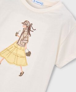 White T shirt with an illustration of a woman in a beige jacket and yellow skirt walking with a drink and a purse