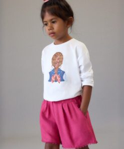 Young girl standing in a white sweatshirt with a back-view anatomy print, pink shorts, and a pink bow in her hair.