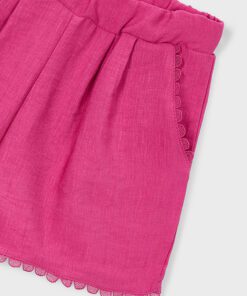 Close up of bright pink knit shorts with an elastic waist and scalloped lace trim along the hem and pocket edge