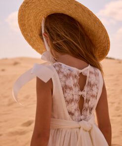 Girl in a white lace dress with a large straw hat seen from behind in a sandy desert landscape