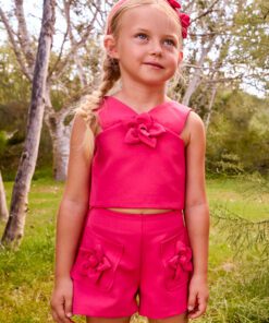 Young girl in a bright pink two piece outfit with flower decorations standing in a park like setting