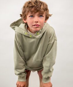 Young boy with messy blond hair wearing a light green hoodie leaning forward and looking upward with a neutral expression