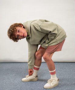 Boy in a gray hoodie and pink shorts bends to tie his shoe on a blue carpeted floor